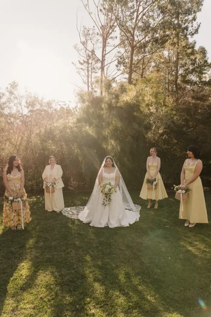 Bride and bridesmaids spaced across a lawn in golden afternoon light