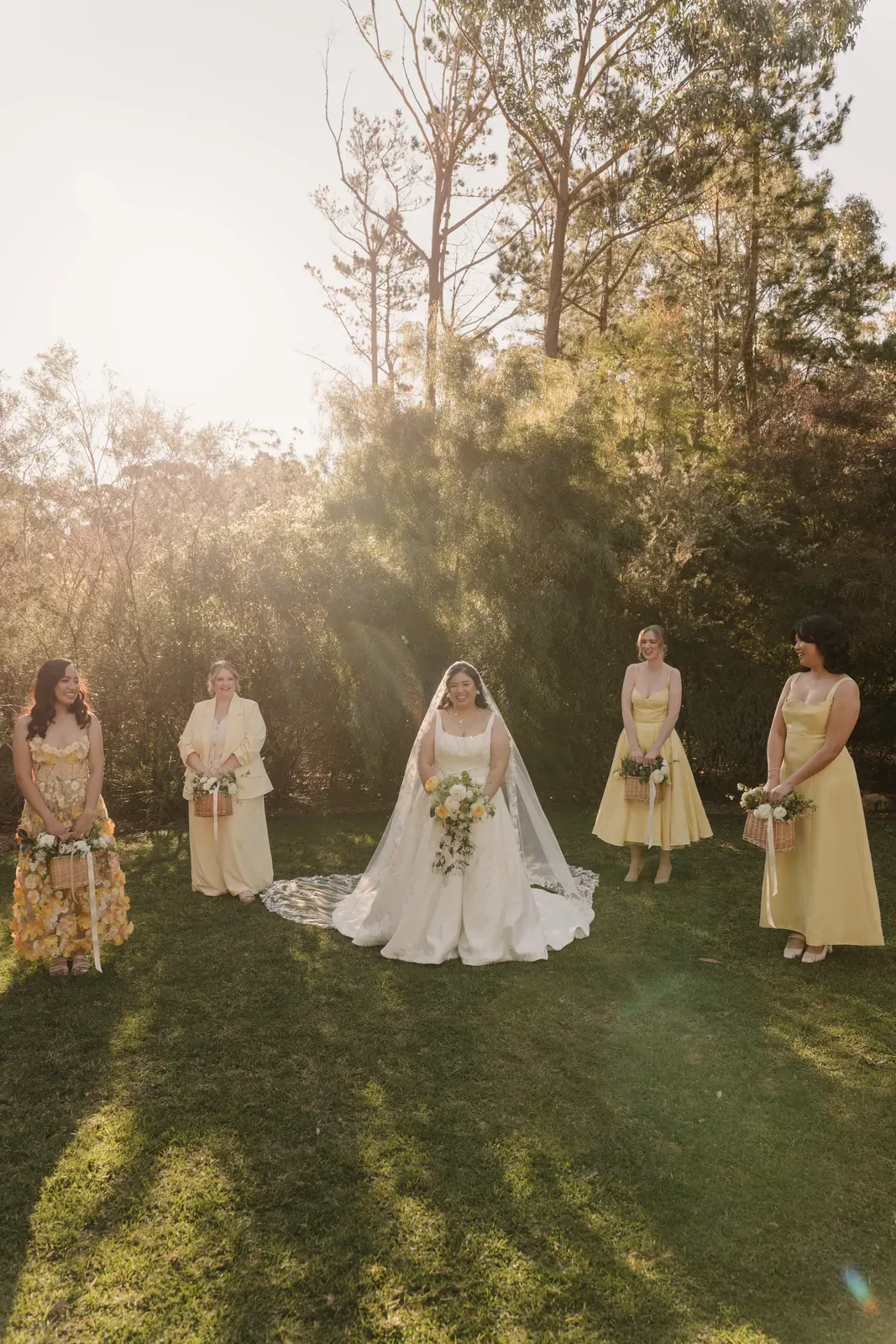 Bride and bridesmaids spaced across a lawn in golden afternoon light