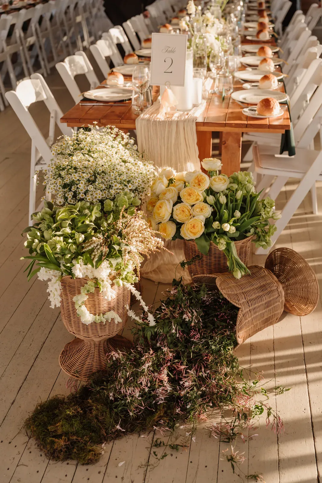 Long reception table with yellow and white urn arrangements set on the floor beside it