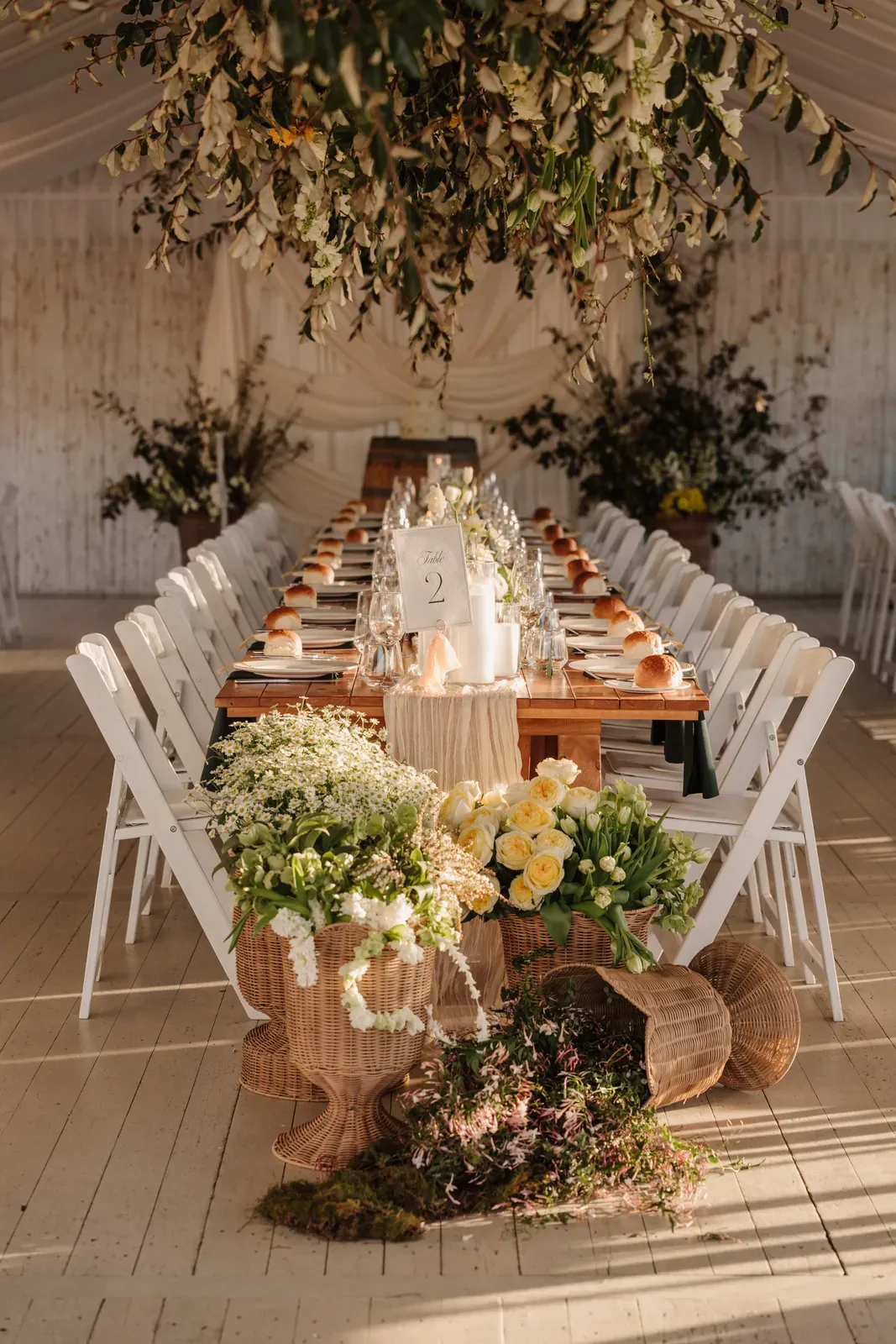 Head table beneath a suspended greenery cloud, white chairs down both sides