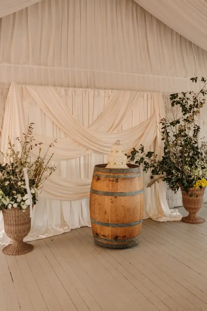 Wine barrel between tall urn arrangements against draped marquee walls