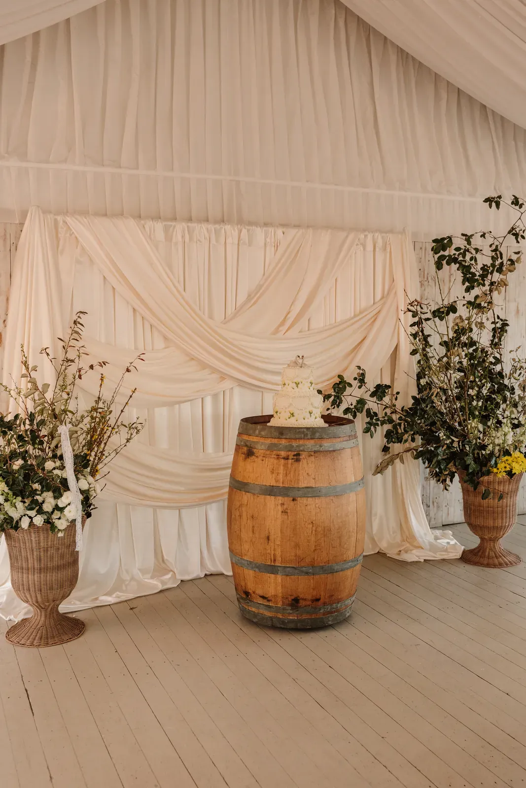 Wine barrel between tall urn arrangements against draped marquee walls