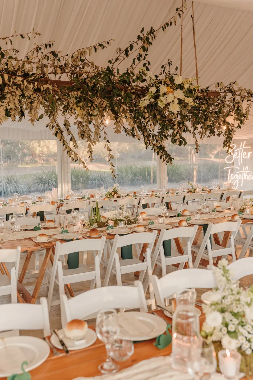 Marquee tables under a hanging greenery installation in window light