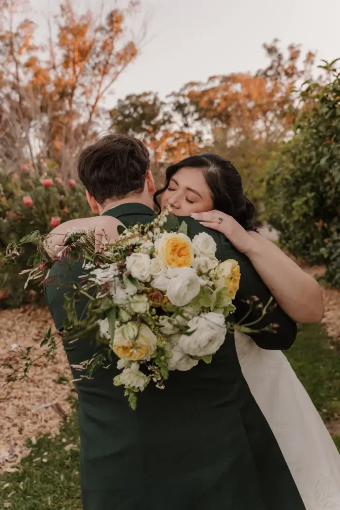 Bride embracing her groom while holding a yellow and white bouquet