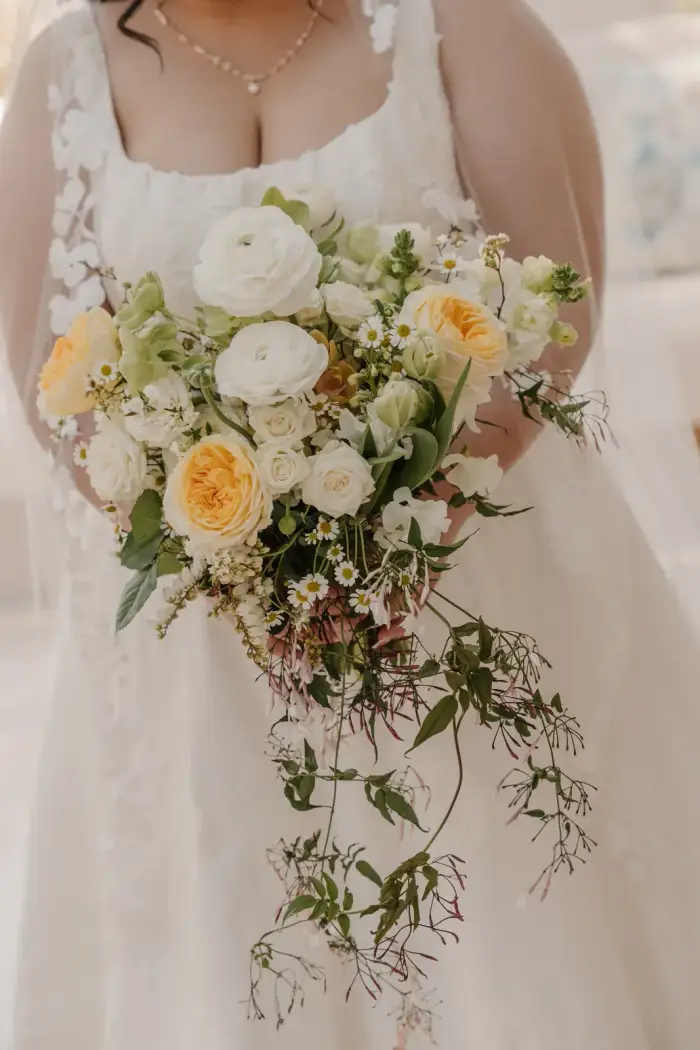Close-up of the bride's white and yellow bouquet with trailing greenery