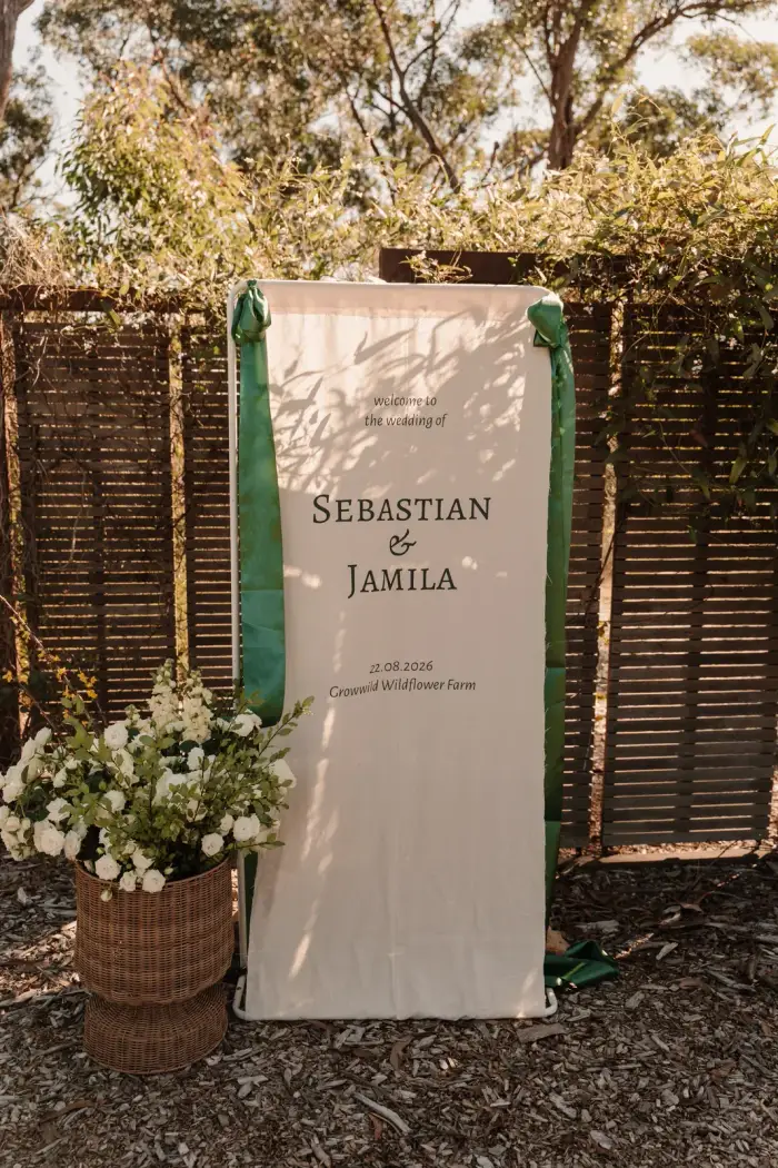 Wedding welcome sign on a timber screen with basket arrangements at its base