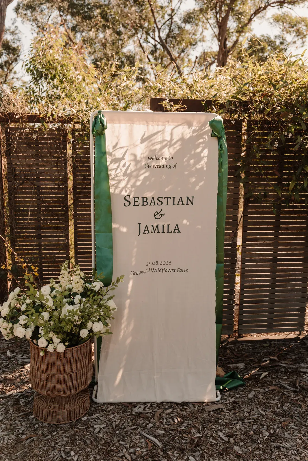 Wedding welcome sign on a timber screen with basket arrangements at its base