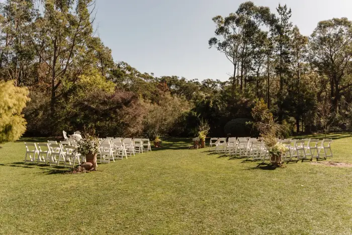 Garden ceremony lawn lined with white chairs and aisle flower arrangements