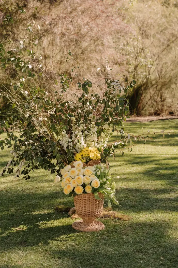 Urn arrangement of yellow roses standing under a flowering tree