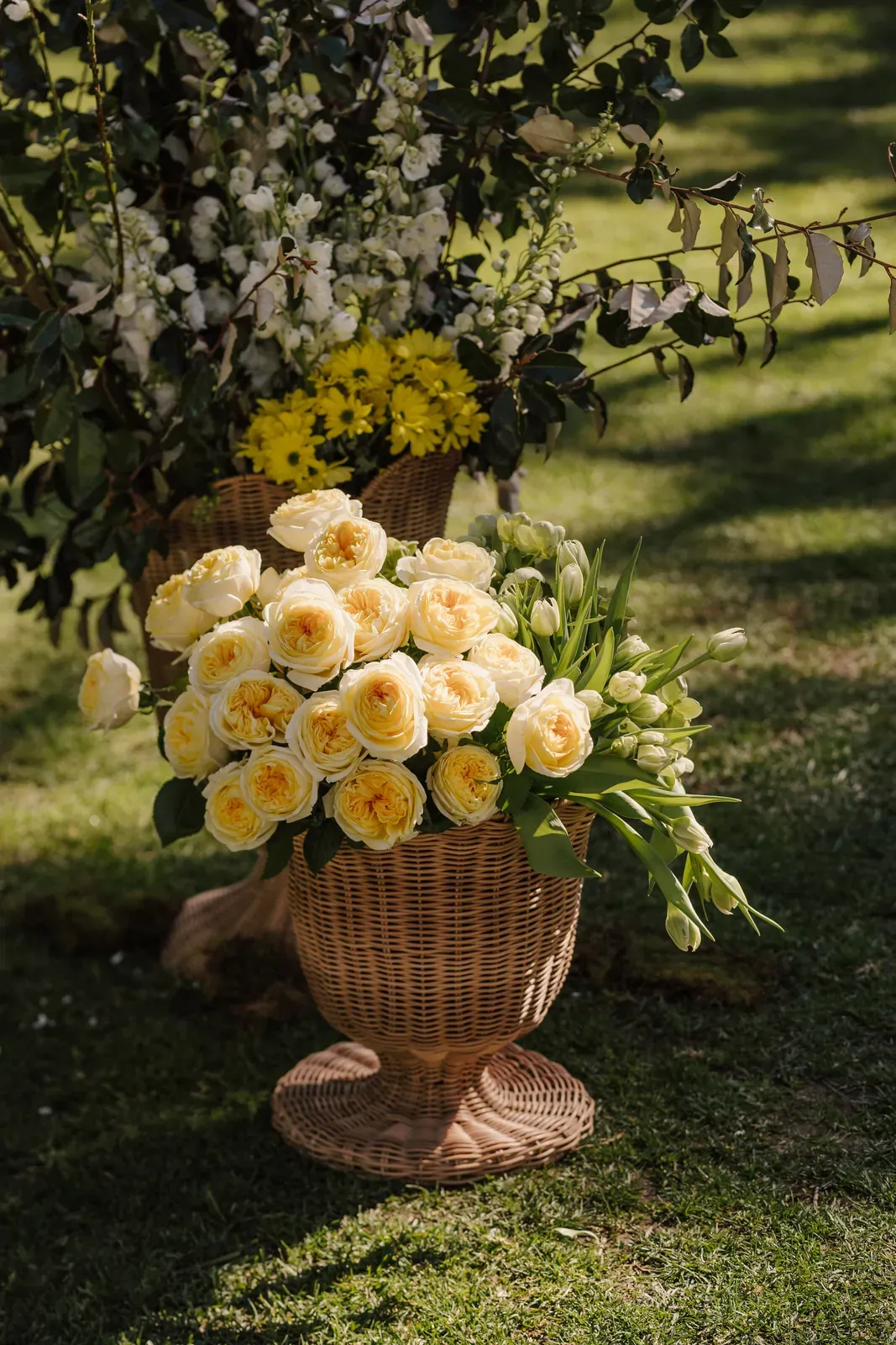 Yellow roses and tulips in a woven urn beneath hanging greenery
