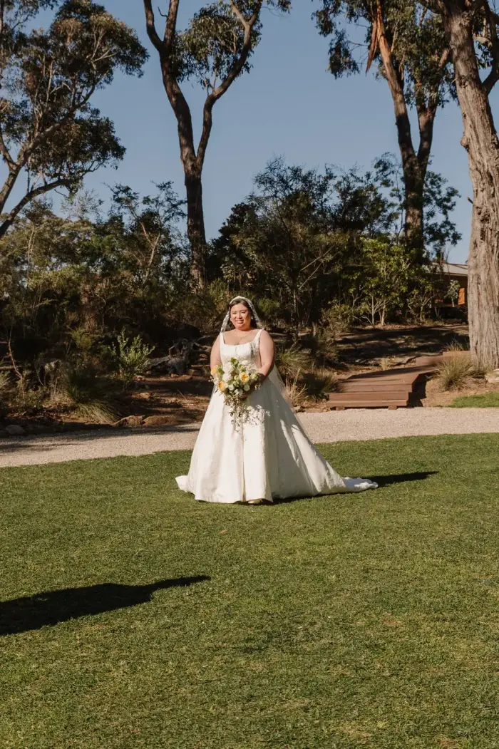 Bride on the lawn holding her bouquet among the gum trees