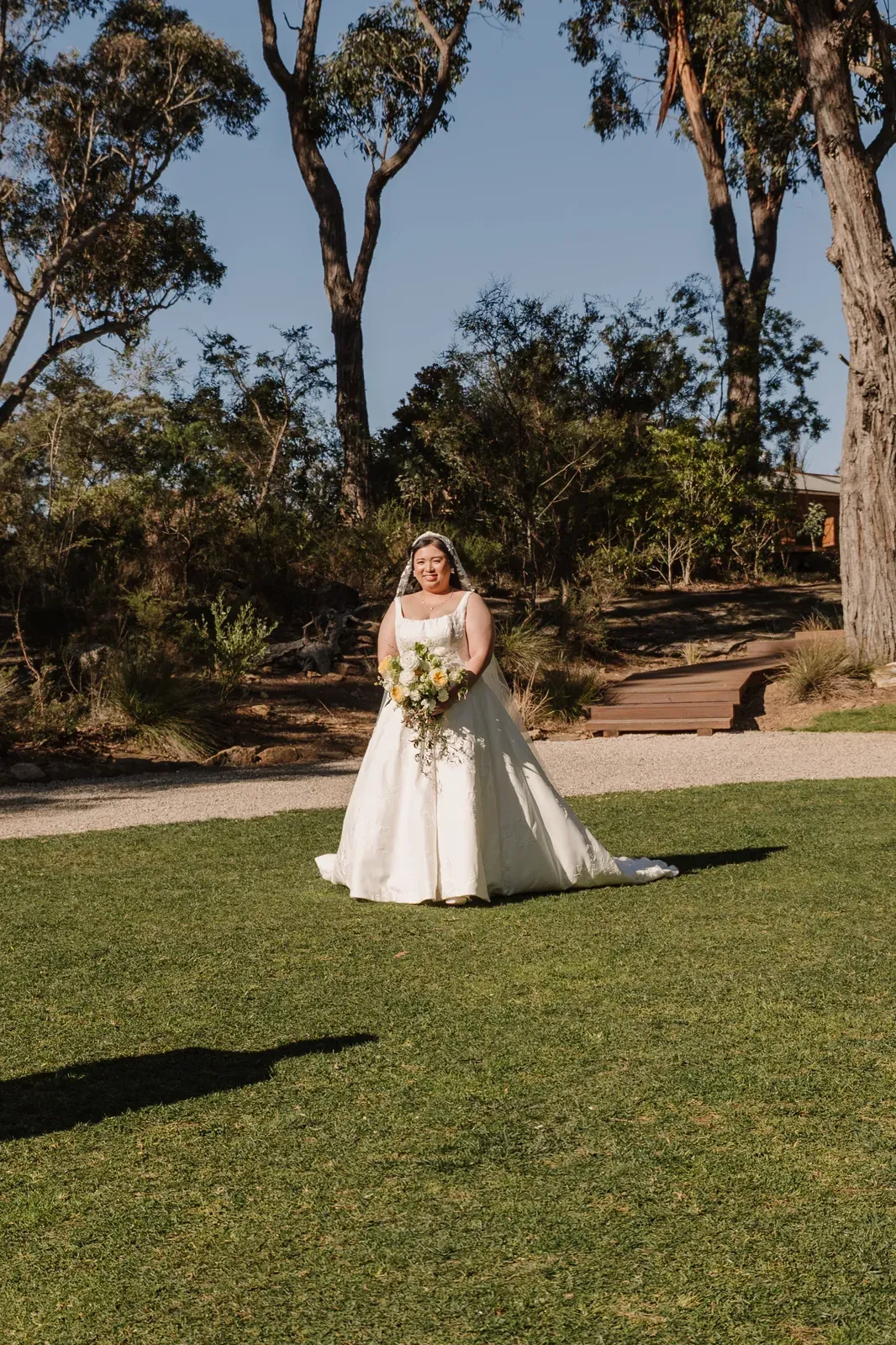 Bride on the lawn holding her bouquet among the gum trees