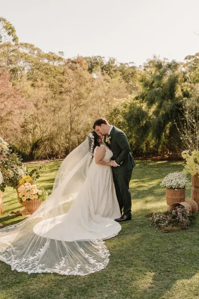 Bride and groom kissing on the lawn with her veil sweeping behind them