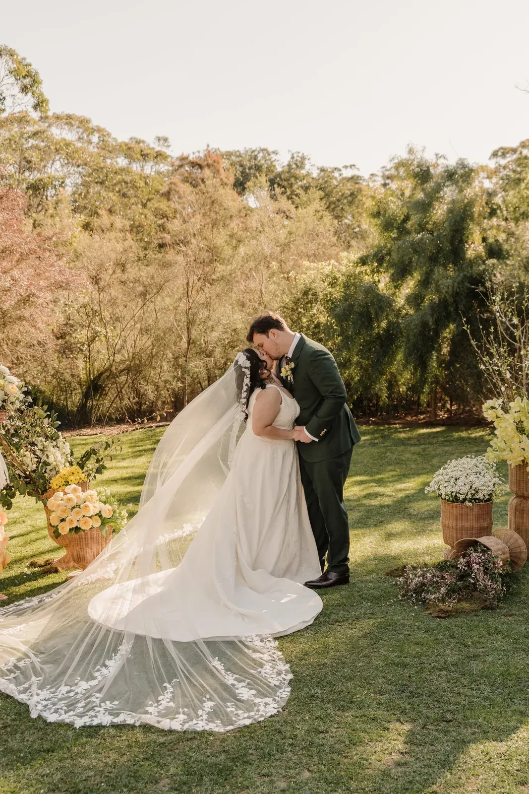 Bride and groom kissing on the lawn with her veil sweeping behind them