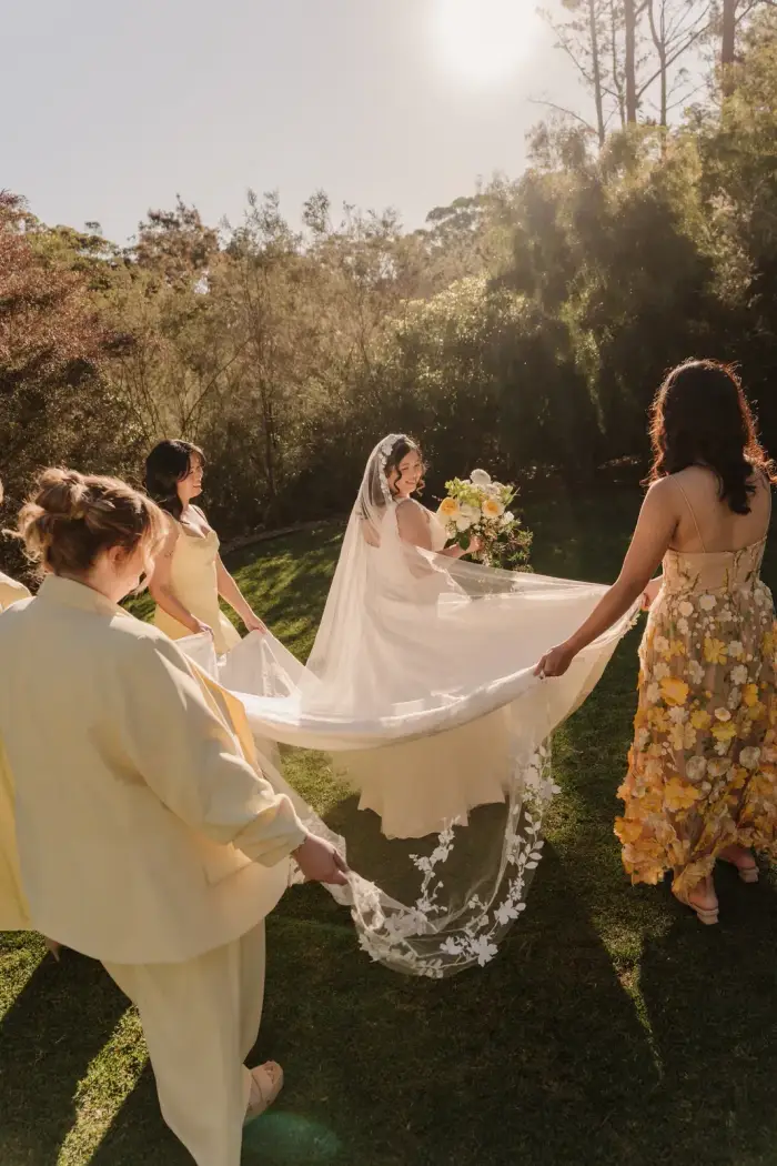 Bridal party lifting the bride's veil in the garden at sunset