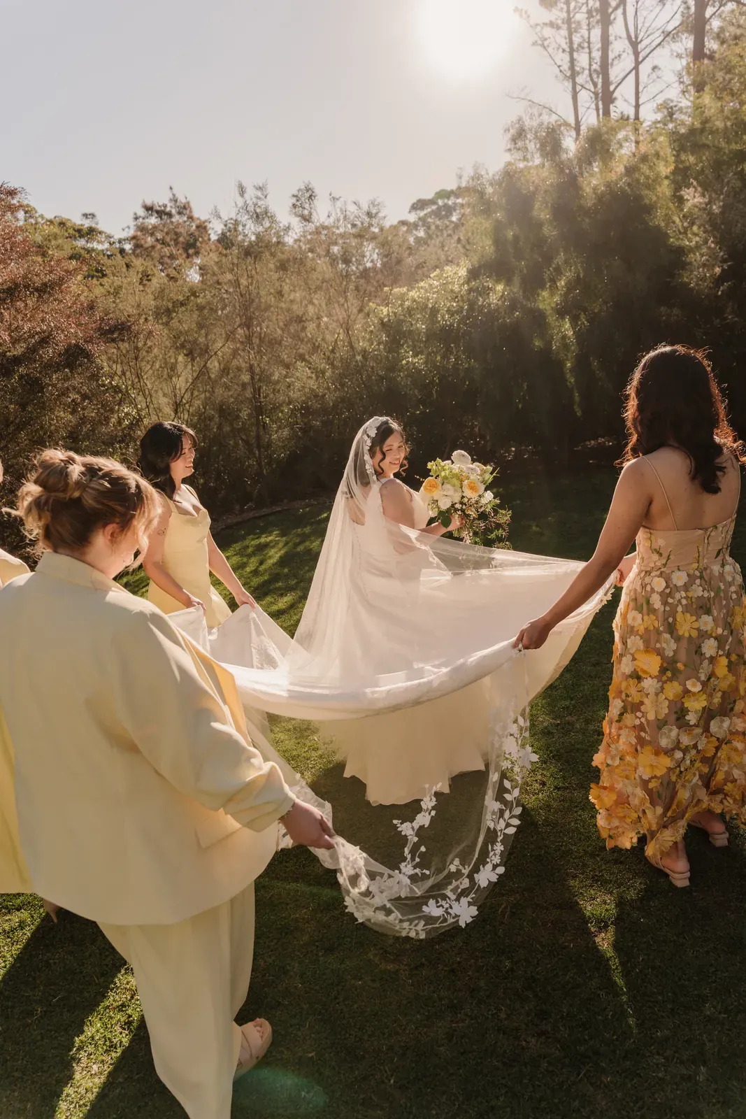 Bridal party lifting the bride's veil in the garden at sunset
