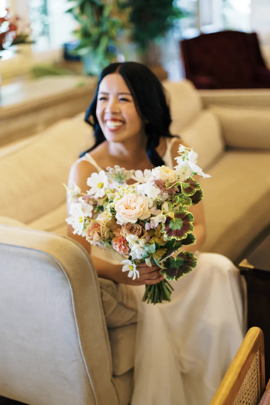 Bride laughing on a couch, holding a pastel bridal bouquet