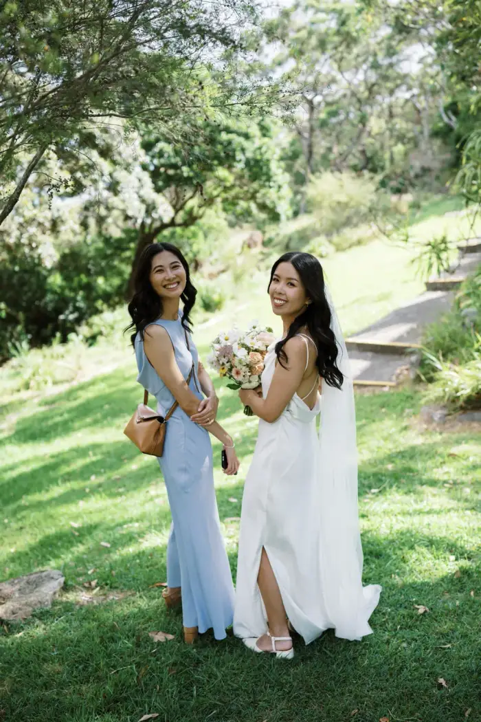 Two bridesmaids in pale blue and white dresses smiling in a garden