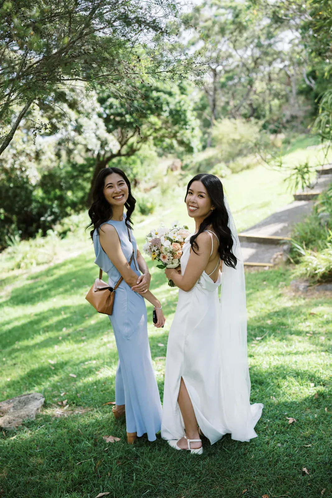 Two bridesmaids in pale blue and white dresses smiling in a garden