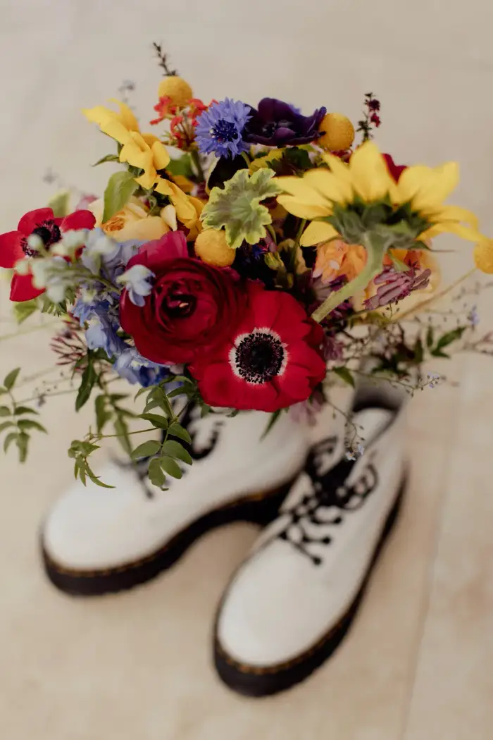 Colourful wildflower bouquet with sunflowers, ranunculus and anemones displayed in white boots