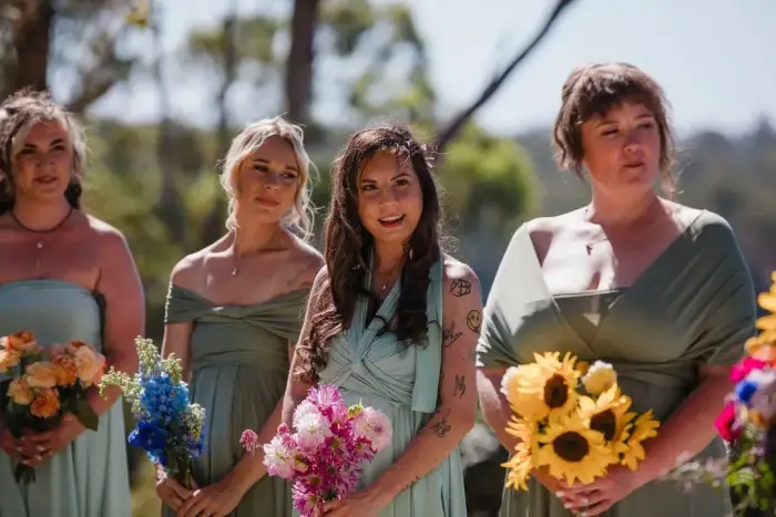 Bridesmaids in sage green dresses holding mixed wildflower bouquets