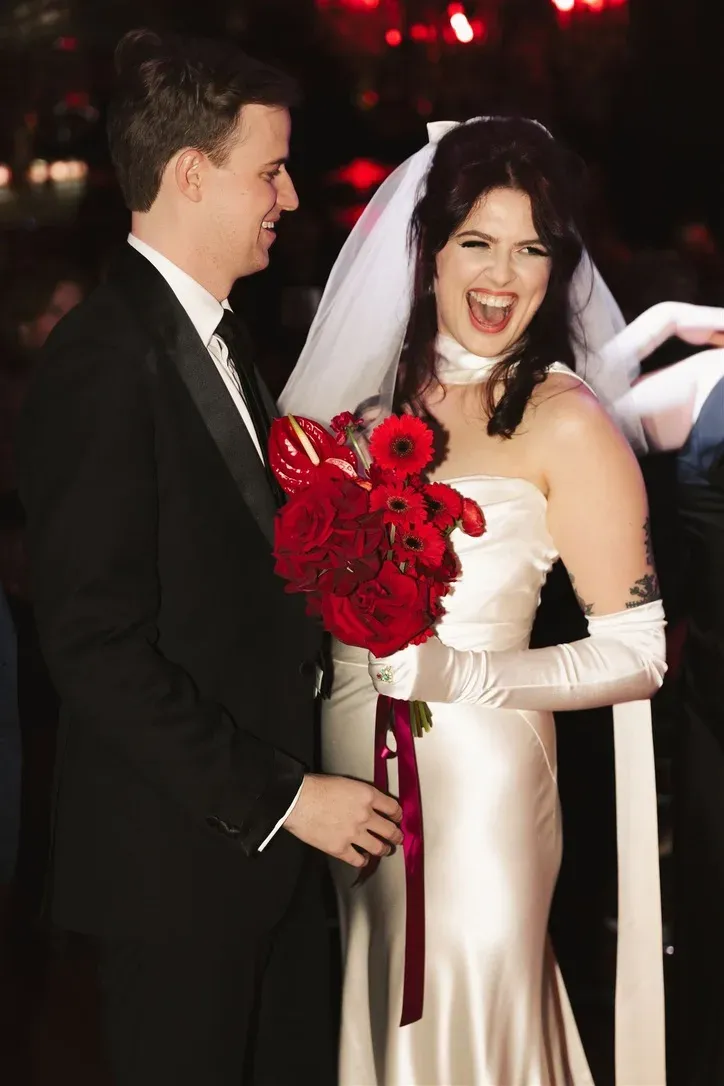 Bride and groom laughing together, bride holding red roses