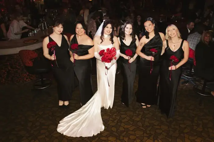 Bride with her bridesmaids in black dresses, all holding red rose bouquets