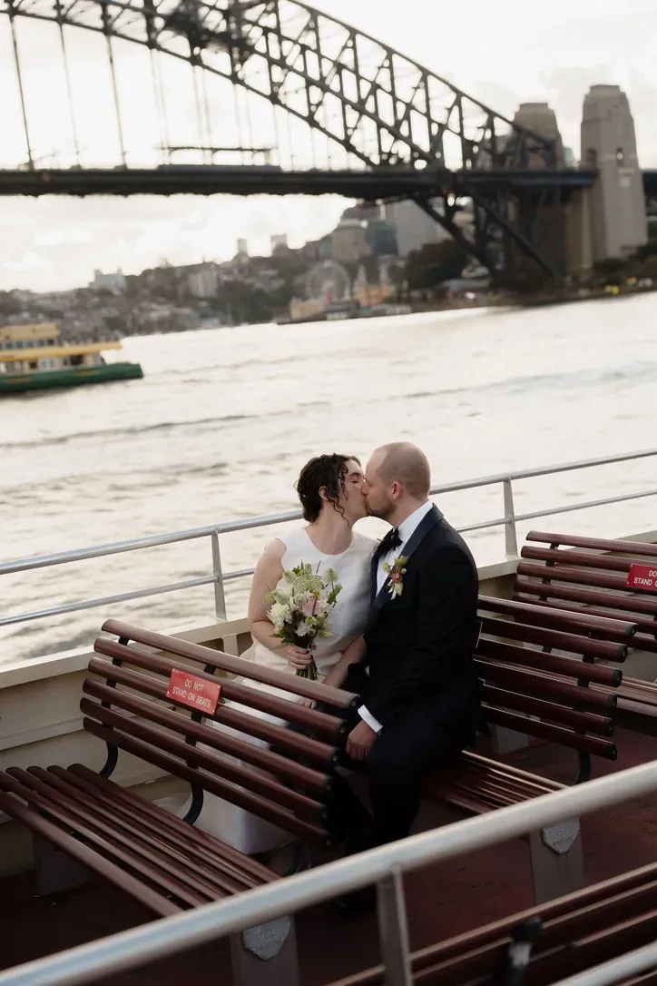 Bride and groom kissing on a ferry with the Sydney Harbour Bridge behind them